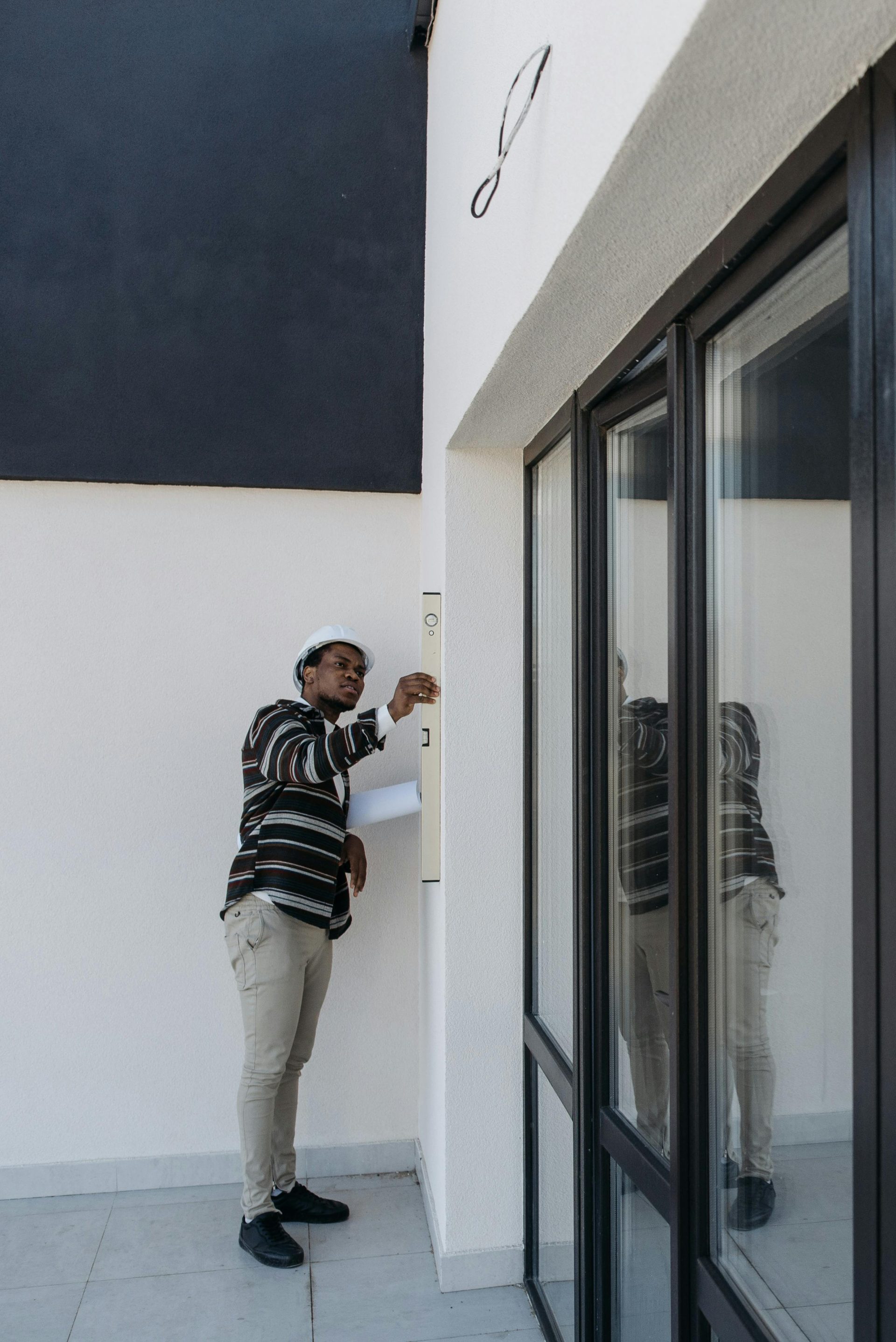 Architect with hard hat inspecting glass doors in a modern building outdoors.